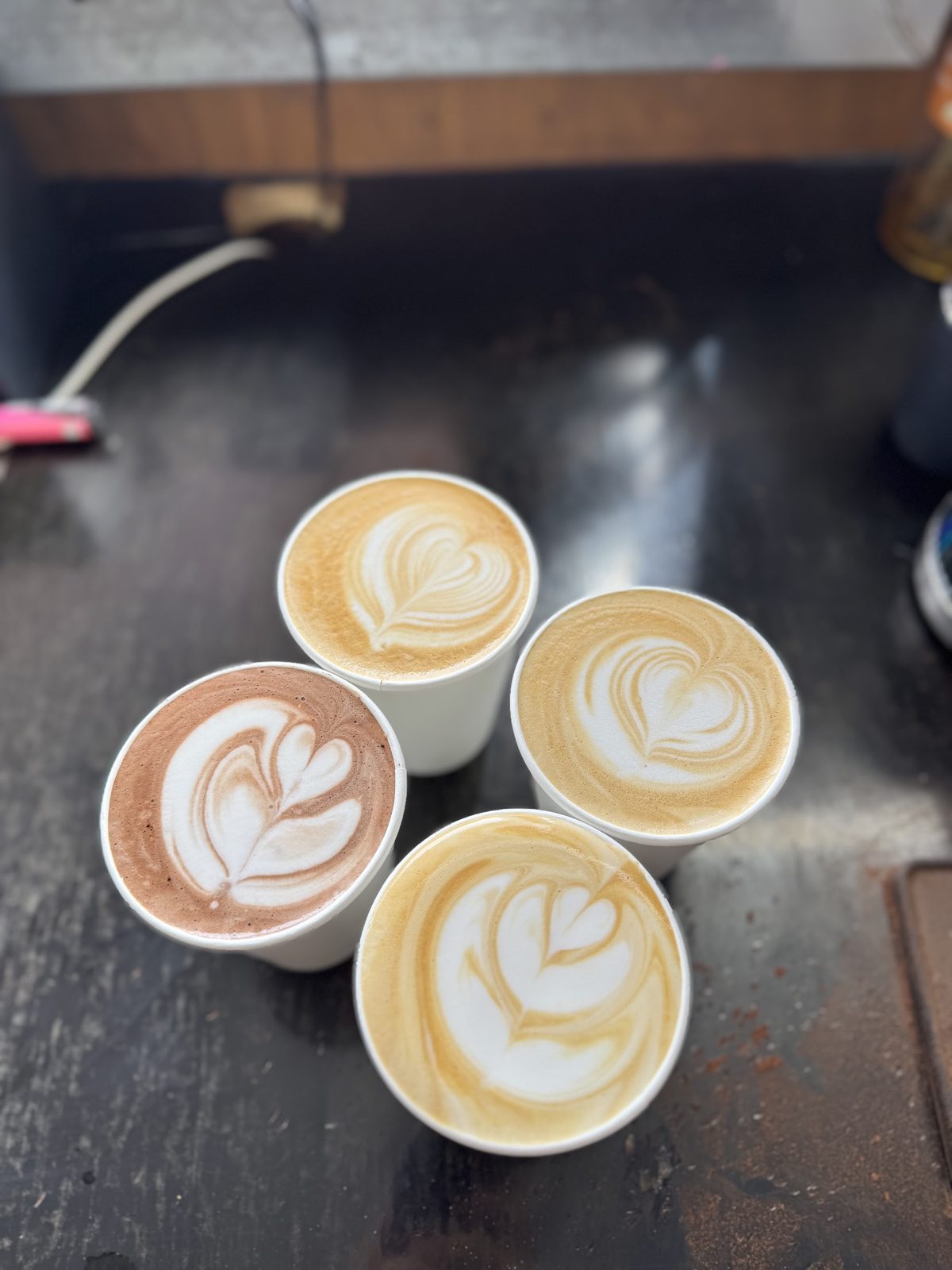 Four takeaway coffees with heart and rosette latte art