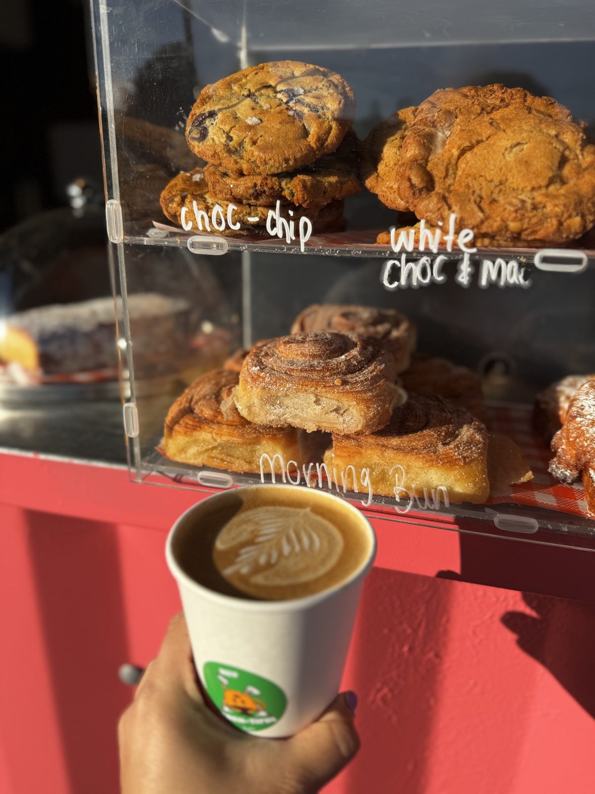 The pastry case with choc chip cookies, white choc and macadamia cookies and morning buns, and a coffee held up in front