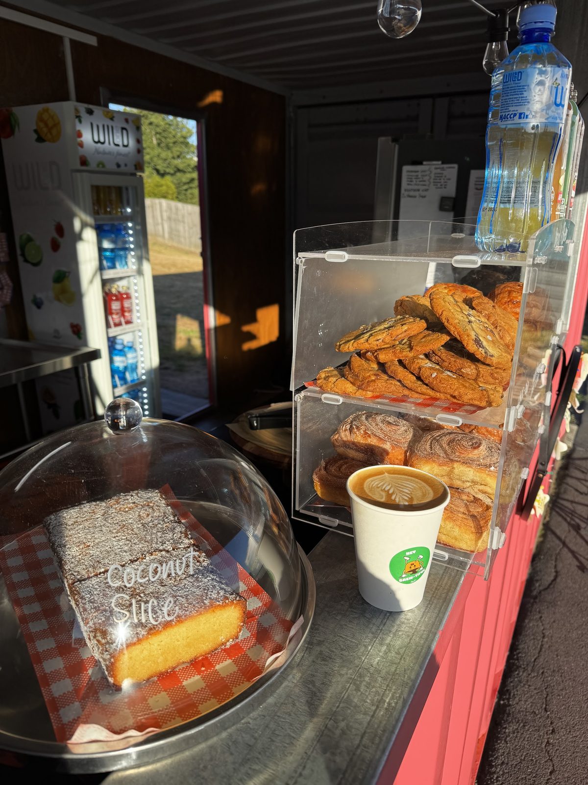 Inside the container: the drinks fridge, cookies in the case and coconut slice under a glass dome