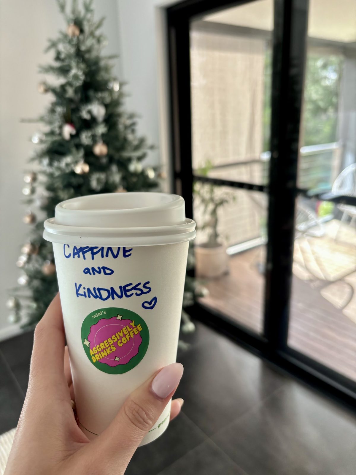 A Sejal's takeaway cup with 'caffine and kindness' written on it in marker